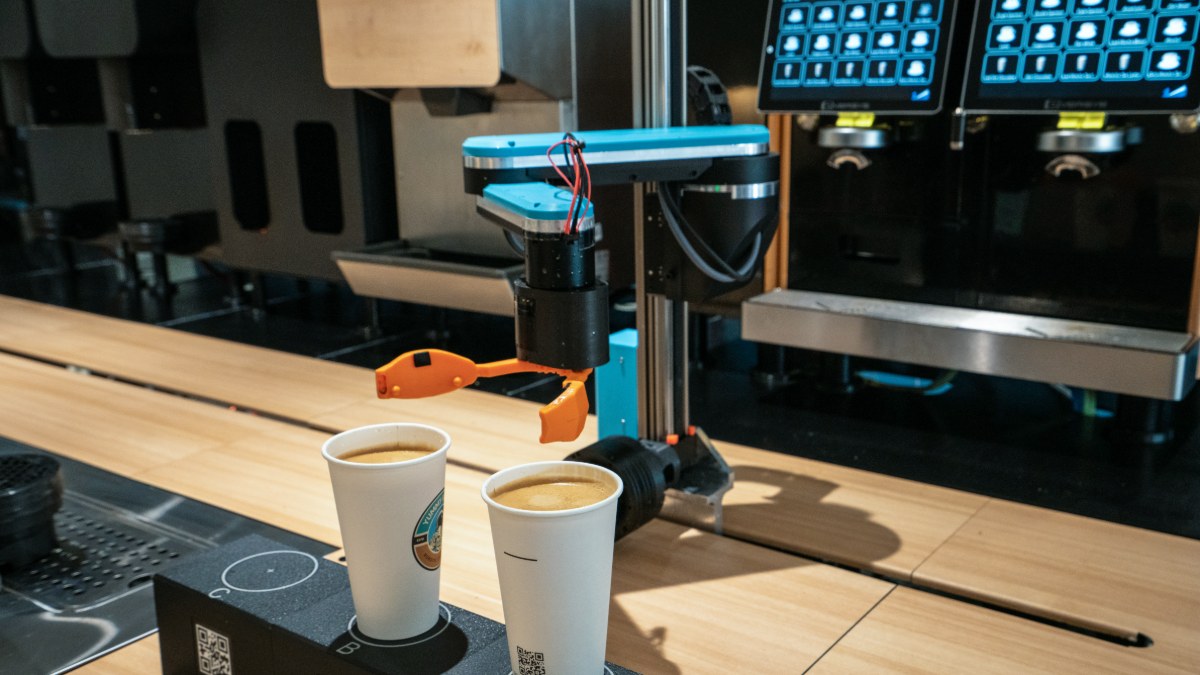 Robotic arm with an orange gripper positioning two cups under the espresso heads